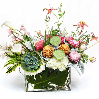 Mixed floral arrangement in a clear square vase with lotus pods and succulents