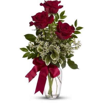 Three red roses in a clear glass vase with a burgundy ribbon