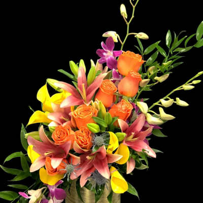 Orange roses with pink lilies and yellow calla lilies in a gold vase