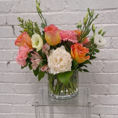 Mixed bouquet of pink, orange, and white flowers in a glass vase