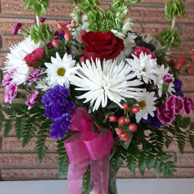 Mixed bouquet with a red rose, white daisies, and purple flowers in a glass vase