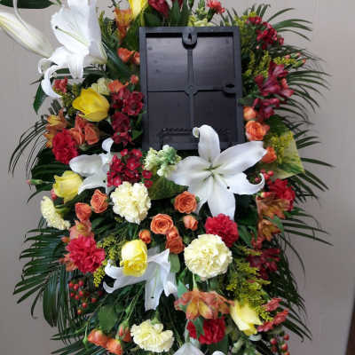 Standing funeral wreath with white lilies, roses, and carnations around a photo frame