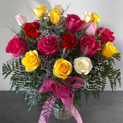 Mixed bouquet of colorful roses in a glass vase with a pink ribbon