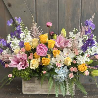 Large mixed flower arrangement in a wooden box with pink, yellow, purple, and white blooms