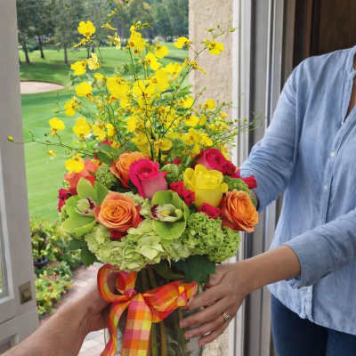 Colorful bouquet of roses and yellow orchids in a glass vase with ribbon