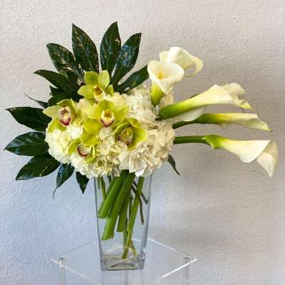 White calla lilies and green orchids in a clear glass vase