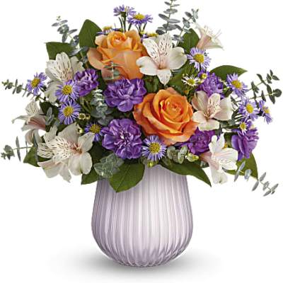 Bouquet of orange roses, purple daisies, and white lilies in a lavender vase