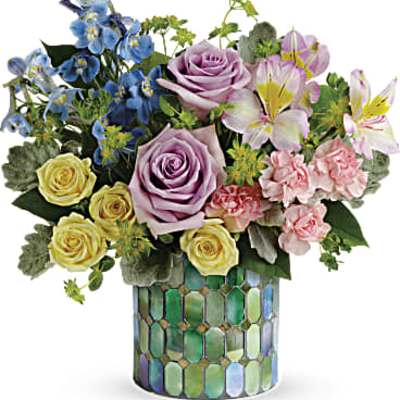 Mixed bouquet of roses, lilies, and blue flowers in a mosaic vase