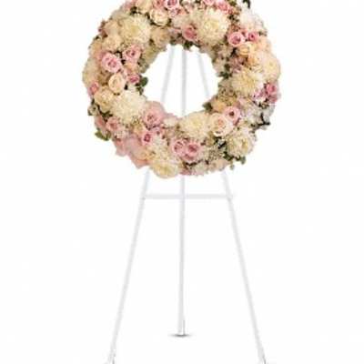 Round floral wreath of pale pink and cream flowers on a white stand