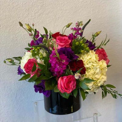 Mixed bouquet of roses, hydrangeas, and purple blooms in a black vase