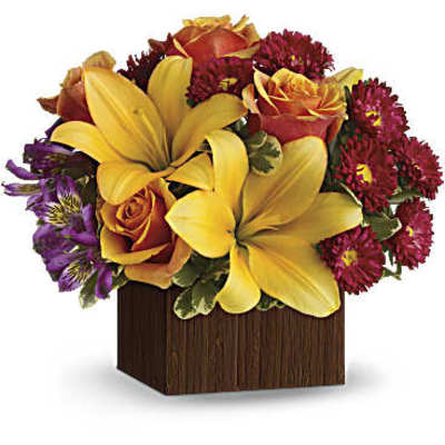 Bouquet of yellow lilies, orange roses, and red daisies in a wooden cube vase