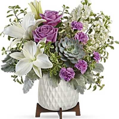 Purple roses and white lilies arranged in a white vase with succulents