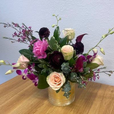 Mixed bouquet of roses, orchids, and dark blooms in a gold vase