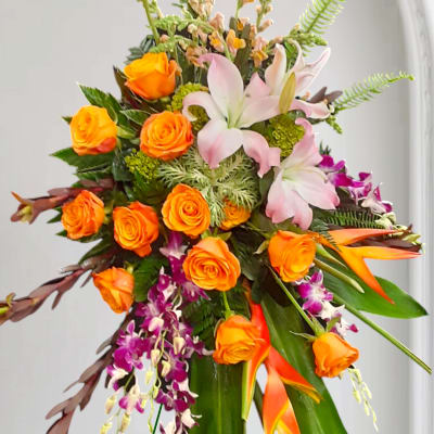 Orange roses and pink lilies with purple orchids in a tall arrangement
