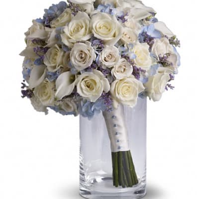 White rose bouquet with blue accents in a clear glass vase