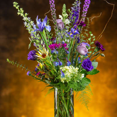 Tall mixed bouquet in a clear glass vase with purple and blue flowers