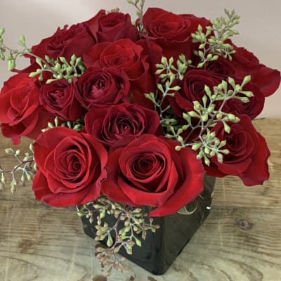 Red roses arranged in a black square vase with green filler sprigs