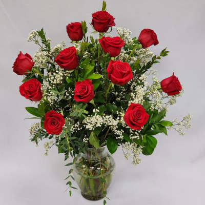 Red roses arranged in a clear glass vase with white filler flowers