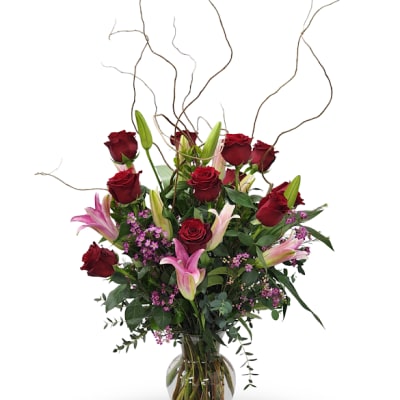 Red roses and pink lilies in a clear glass vase with curly branches