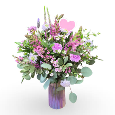 Pink and lavender mixed bouquet in a purple glass vase with a heart pick
