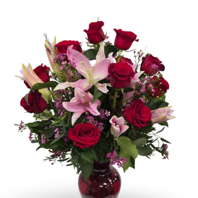 Red roses and pink lilies arranged in a red glass vase