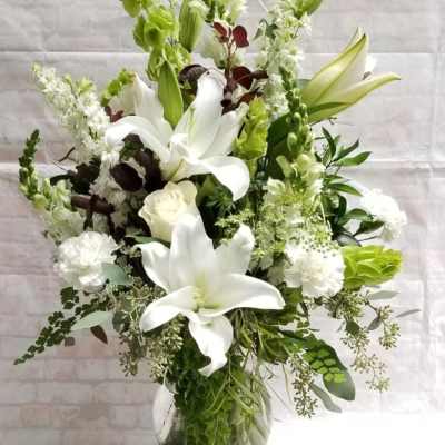 White lilies and green blooms in a clear glass vase
