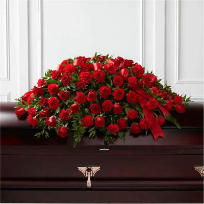 Red rose and carnation casket spray with ribbon on a dark wood casket