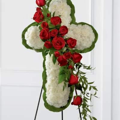 Standing floral cross of white blooms with cascading red roses on a metal easel.