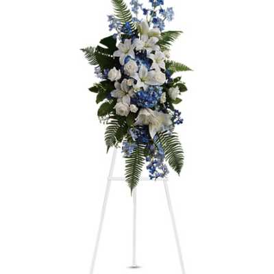 Standing spray of white lilies and roses with blue delphinium on a white metal easel