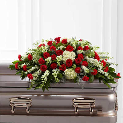 Red and white casket spray with roses, carnations, hydrangeas, and snapdragons atop a metallic casket