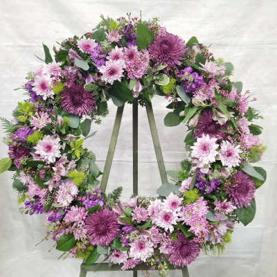 Large purple and pink floral wreath on a wooden easel against a light backdrop