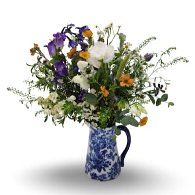 Mixed bouquet of purple, white, and orange flowers in a blue-and-white pitcher vase