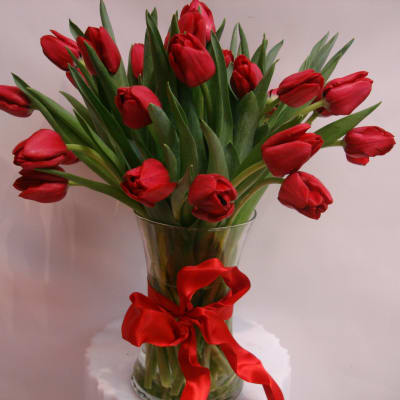 Red tulips arranged in a clear glass vase with a red ribbon