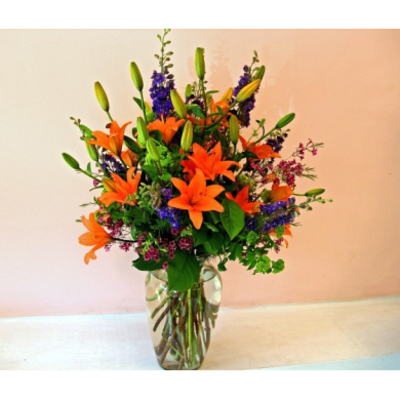 Orange lilies and purple flowers in a clear glass vase