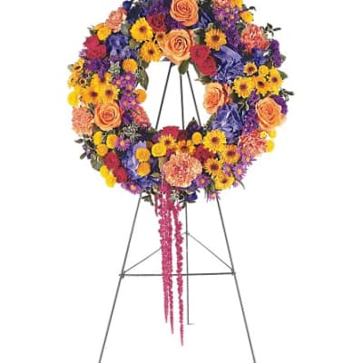 Colorful funeral wreath on a metal stand with hanging pink ribbon