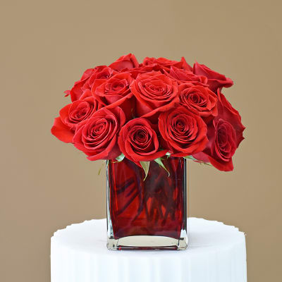 Red roses arranged in a square glass vase with red water