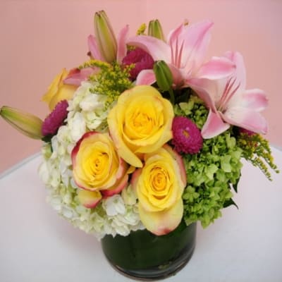 Bouquet of yellow roses, pink lilies, and white hydrangeas in a glass vase