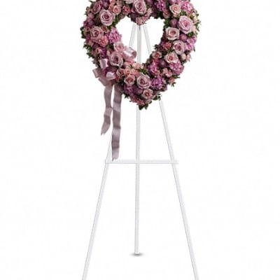 Heart-shaped pink rose wreath on a white stand with ribbon