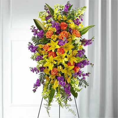 Tall standing spray with yellow lilies, orange roses, and purple and white flowers on a metal easel.