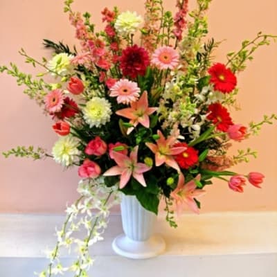 Tall mixed flower arrangement in a white vase with pink, red, and white blooms