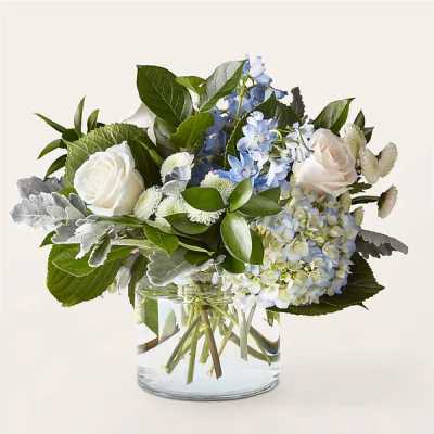 Compact blue and white arrangement with roses and hydrangeas in a clear glass vase