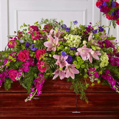 Bright pink and purple casket spray with lilies, roses, and mixed blooms on a wooden casket