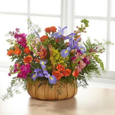 Colorful basket arrangement with orange roses, purple irises, and pink snapdragons.