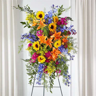 Tall standing spray of sunflowers, orange lilies, and bright mixed flowers on a metal easel