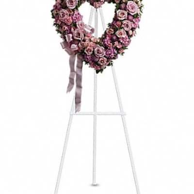 Heart-shaped pink rose wreath on a white stand with ribbon