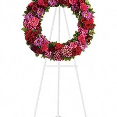 Circular floral wreath on a white easel with red and pink flowers