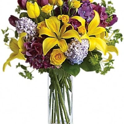 Yellow lilies and purple flowers in a clear glass vase