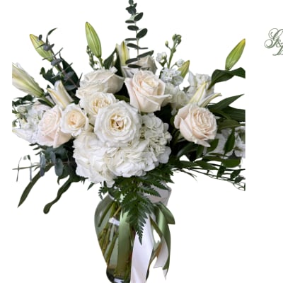 White roses and lilies in a glass vase with greenery