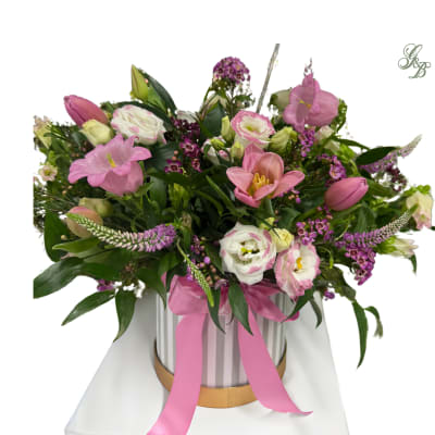 Pink and white mixed flower arrangement in a striped hatbox with a pink ribbon