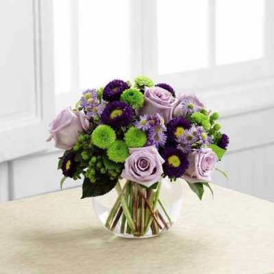 Lavender roses and purple-green pompom flowers in a clear glass vase